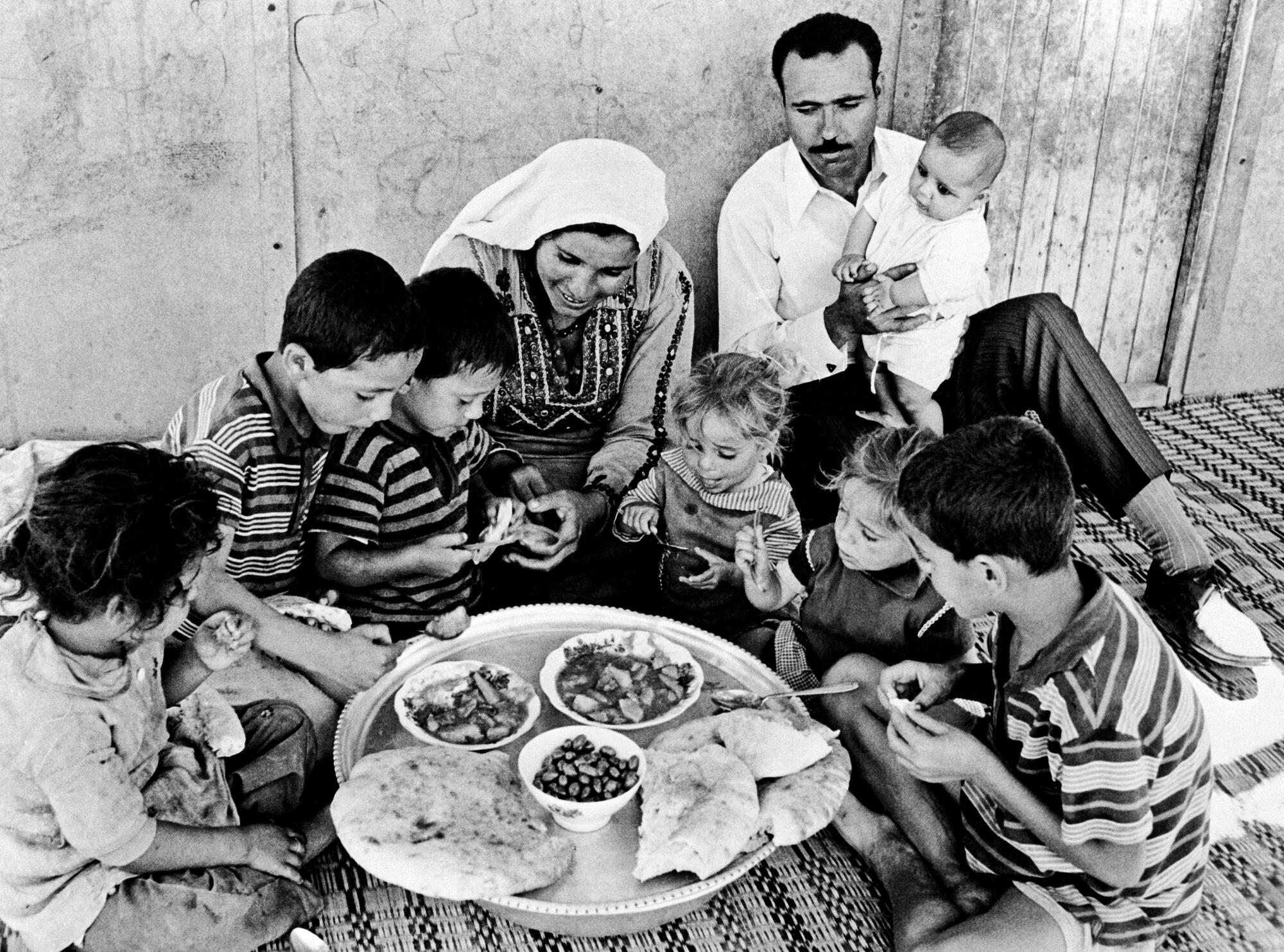 A refugee family makes the most of the limited space in their prefabricated hut in Baqa'a Camp near Amman. As a result of contributions from governments, voluntary organizations and individuals, prefabricated huts offering better protection against the elements than the canvas tents they replaced, have been set up in the emergency camps in East Jordan. [circa 1970]